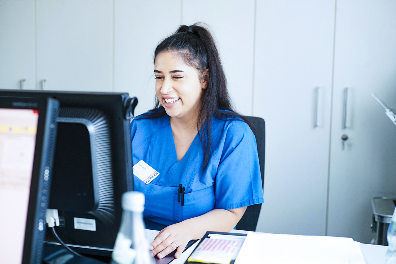 Eine Pflegerin am Schreibtich vor einem Monitor.