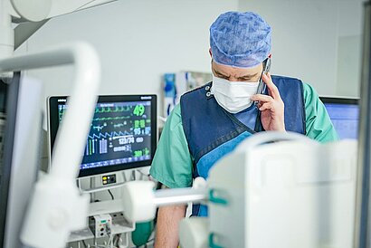 Röntgenarzt mit Mundschutz telefonierend im Röntgenraum.